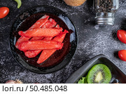 Crab stick put on a black plate with raw salmon, tomatoes, kiwi, shallots and sweet peppers on the black cement floor. Стоковое фото, агентство Ingram Publishing / Фотобанк Лори