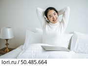 That woman sat on the bed, raised her hand, and put the laptop on the pillow. Стоковое фото, агентство Ingram Publishing / Фотобанк Лори