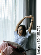 A woman in a white shirt sitting on the bed and raising both arms. Стоковое фото, агентство Ingram Publishing / Фотобанк Лори