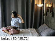 A woman in a white shirt sitting on the bed and raising both arms. Стоковое фото, агентство Ingram Publishing / Фотобанк Лори