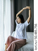A woman in a white shirt sitting on the bed and raising both arms. Стоковое фото, агентство Ingram Publishing / Фотобанк Лори