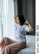 A woman in a white shirt sitting on the bed and raising both arms. Стоковое фото, агентство Ingram Publishing / Фотобанк Лори