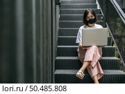 Women wearing masks and playing laptops on the stairs. Selective focus. Стоковое фото, агентство Ingram Publishing / Фотобанк Лори