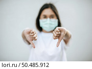 The woman is wearing a mask and pointing her thumb down. Стоковое фото, агентство Ingram Publishing / Фотобанк Лори