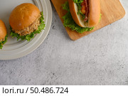 Selective focus hamburger placed in white dish beautifully and hotdog on wooden cutting board, blurred lettuce in weave basket, copy space. Стоковое фото, агентство Ingram Publishing / Фотобанк Лори