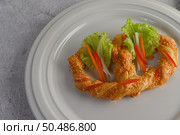 Freshly baked soft pretzel with generous sprinkling of coarse salt and sesame on white dish, decorate with lettuce and carrot beautifully, copy space. Стоковое фото, агентство Ingram Publishing / Фотобанк Лори
