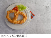 Top View Freshly baked soft pretzel with generous sprinkling of coarse salt and sesame on white dish, decorate with tomato sliced, lettuce and carrot beautifully, copy space. Стоковое фото, агентство Ingram Publishing / Фотобанк Лори