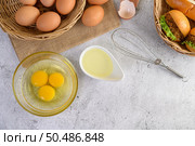 Top view with yolk in glass bowl and in wicker basket, hamburgers and hotdog with slice tomato and lettuce in weave basket, oil in cup and egg whisk placed nearly. Стоковое фото, агентство Ingram Publishing / Фотобанк Лори