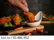 Hand holding crispy fried chicken dipped in tomato sauce. Selective focus. Стоковое фото, агентство Ingram Publishing / Фотобанк Лори