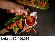 Hand holding crispy fried chicken dipped in tomato sauce. Selective focus. Стоковое фото, агентство Ingram Publishing / Фотобанк Лори