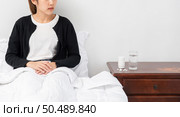 An uncomfortable woman sits on the bed and has medicine on the table. Стоковое фото, агентство Ingram Publishing / Фотобанк Лори