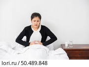 A woman sitting in bed with abdominal pain and pressing her hand on her stomach. Стоковое фото, агентство Ingram Publishing / Фотобанк Лори