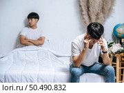 Two young men were angry on the bed and the other sat at the edge of the bed and was stressed. Стоковое фото, агентство Ingram Publishing / Фотобанк Лори