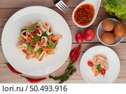 Stir-fried noodles with squid, tomatoes, peppers, chives, Celery and crab sticks in a white plate on a wooden floor. Стоковое фото, агентство Ingram Publishing / Фотобанк Лори