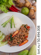 Stir fried pork with basil, fried egg in a white dish with cucumber, galangal, garlic, lemon and chilli on a wooden floor. Стоковое фото, агентство Ingram Publishing / Фотобанк Лори