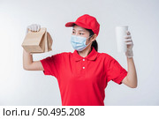 Image of a happy young delivery man in red cap blank t-shirt uniform face mask gloves standing with empty brown craft paper packet isolated on light gray background studio, Service during pandemic coronavirus virus covid-19 concept. Стоковое фото, агентство Ingram Publishing / Фотобанк Лори
