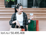 Portrait beautiful woman place eyeglasses on head holding shopping bags in hand sit on stairs of mall, she smile and show credit cards in hand,  Lifestyle and shopping concept. Стоковое фото, агентство Ingram Publishing / Фотобанк Лори