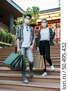 Cheerful Young couple in mask holding multiple paper shopping bag going down stairs of large shopping mall and pretty woman show credit card in hand,  Lifestyle and shopping concept, copy space. Стоковое фото, агентство Ingram Publishing / Фотобанк Лори
