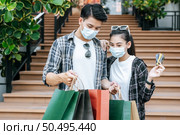 Cheerful Young couple holding multiple paper shopping bag going down stairs of large shopping mall and pretty woman show credit card in hand, They look inside bag with excited. Стоковое фото, агентство Ingram Publishing / Фотобанк Лори