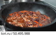 Cast iron pot simmering seasoned meat, releasing fragrant steam alongside chopped carrots, revealing rustic cooking method with deep culinary warmth and traditional flavor. Стоковое видео, видеограф Данил Руденко / Фотобанк Лори