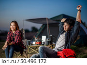 Selective focus Handsom man sitting on chair and streching arms near his girlfriend at front of camping tent, They are smile with happiness and freshness when relaxing in nature. Стоковое фото, агентство Ingram Publishing / Фотобанк Лори