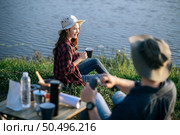Cheerful Young backpacker couple wearing trekking hat sitting near lake with coffee set and making fresh coffee grinder while camping trip on summer vacation. Стоковое фото, агентство Ingram Publishing / Фотобанк Лори