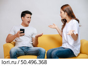 young couple arguing while handsome man using mobile phone on sofa in living room at home. husband addict On Mobile Phone Ignoring her, upset couple, family issues and relationship concept. Стоковое фото, агентство Ingram Publishing / Фотобанк Лори