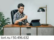 Happily Young handsome man with new normal, Stay at home and works from home on digital tablet and use smartphone during self-isolation and quarantine covid-19 coronavirus outbreak. Стоковое фото, агентство Ingram Publishing / Фотобанк Лори