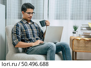 Portrait of smiling handsome man in glasses relaxing with coffee, using technology of laptop computer to working from home during self-isolation and quarantine covid-19 coronavirus outbreak. Стоковое фото, агентство Ingram Publishing / Фотобанк Лори
