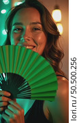 A woman with a green fan smiling in a dimly lit venue, fairy lights creating bokeh effects in background, music laser show on background. Стоковое AI-видео, аниматор Sergey Grishin / Фотобанк Лори