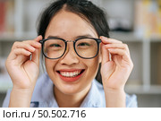 Protrait young asian woman happy positive smile and use hand touch eyeglasses and looking at camera at living room. Стоковое фото, агентство Ingram Publishing / Фотобанк Лори