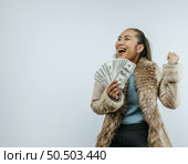 Portrait of successful Asian woman with a fur coat holding money in hand ,smiling and raising arm, standing over background in studio with copy space. Advertising concept. Стоковое фото, агентство Ingram Publishing / Фотобанк Лори