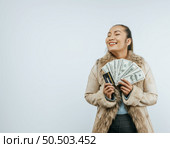 Portrait of successful Asian woman with a fur coat holding money and card, smiling and closing eyes, standing over background in studio with copy space. Стоковое фото, агентство Ingram Publishing / Фотобанк Лори
