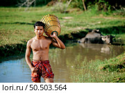 Portrait Young man topless use bamboo fishing trap to catch fish for cooking, Asian young farmer man in rural lifestyle, blurred buffalo is soaking in the swamp. in background. Стоковое фото, агентство Ingram Publishing / Фотобанк Лори