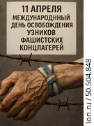 Elderly hand with a striped cloth wristband rests on a barbed wire, symbolizing a historical event. Text above states: "11 апреля Международный день освобождения узников фашистских концлагерей" Стоковое AI-изображение, AI-художник Olga Dmitrieva / Фотобанк Лори