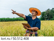 Asian middle aged farmer man wearing straw hat write on clipboard in rice field with smile during keep data with Smart farming Agriculture technology and organic agriculture. Стоковое фото, агентство Ingram Publishing / Фотобанк Лори