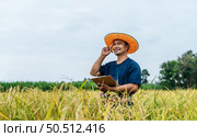 Asian middle aged farmer man wearing straw hat write on clipboard in rice field with smile during keep data with Smart farming Agriculture technology and organic agriculture. Стоковое фото, агентство Ingram Publishing / Фотобанк Лори