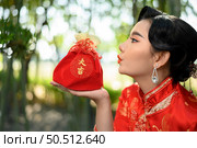 Portrait pretty Asian woman in a Chinese cheongsam posing with Red amulet bag with  Chinese alphabet means good fortune and happinese in bamboo forest background, Chinese New Year concept, copy space. Стоковое фото, агентство Ingram Publishing / Фотобанк Лори