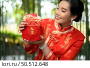 Portrait pretty Asian woman in a Chinese cheongsam holding envelopes in Red amulet bag with Chinese alphabet means good fortune and happinese in bamboo forest background, Chinese New Year concept. Стоковое фото, агентство Ingram Publishing / Фотобанк Лори