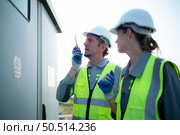 A team of electrical engineers is inspecting an energy storage station of a solar panels in the middle of a hundred acre field of solar panels. Стоковое фото, агентство Ingram Publishing / Фотобанк Лори