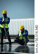 Both of Engineer in charge of solar panel installation The installation of solar energy conversion into electricity for a warehouse is currently being investigated. Стоковое фото, агентство Ingram Publishing / Фотобанк Лори