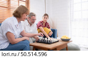 In the living room of the house, an elderly couple sits and relaxes. to begin playing chess together with a chess board with a daughter cheering beside him. Стоковое фото, агентство Ingram Publishing / Фотобанк Лори