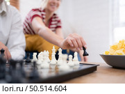 In the living room of the house, an elderly couple sits and relaxes. to begin playing chess together with a chess board with a daughter cheering beside him. Стоковое фото, агентство Ingram Publishing / Фотобанк Лори