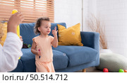 A little girl runs and plays with a small soap bubble that his mother blows for him to play with. In the living room of the house. Стоковое фото, агентство Ingram Publishing / Фотобанк Лори