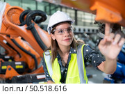 A female engineer installs a program on a robotics arm in a robot warehouse. And test the operation before sending the machine to the customer. Стоковое фото, агентство Ingram Publishing / Фотобанк Лори