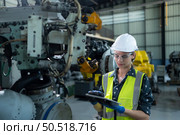 A female engineer installs a program on a robotics arm in a robot warehouse. And test the operation before sending the machine to the customer. Стоковое фото, агентство Ingram Publishing / Фотобанк Лори
