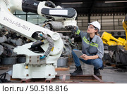 A female engineer installs a program on a robotics arm in a robot warehouse. And test the operation before sending the machine to the customer. Стоковое фото, агентство Ingram Publishing / Фотобанк Лори
