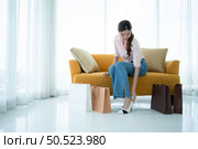 Portrait of young asian woman sitting on sofa in the shop’s VIP lounge with shopping bags. Стоковое фото, агентство Ingram Publishing / Фотобанк Лори