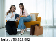 Receptionists use tablets to provide product information to Asian women. on the sofa and shopping bags. Стоковое фото, агентство Ingram Publishing / Фотобанк Лори
