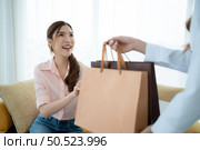 The receptionist delivers the goods that the customer has already purchased to Asian women on the sofa with shopping bags. Стоковое фото, агентство Ingram Publishing / Фотобанк Лори